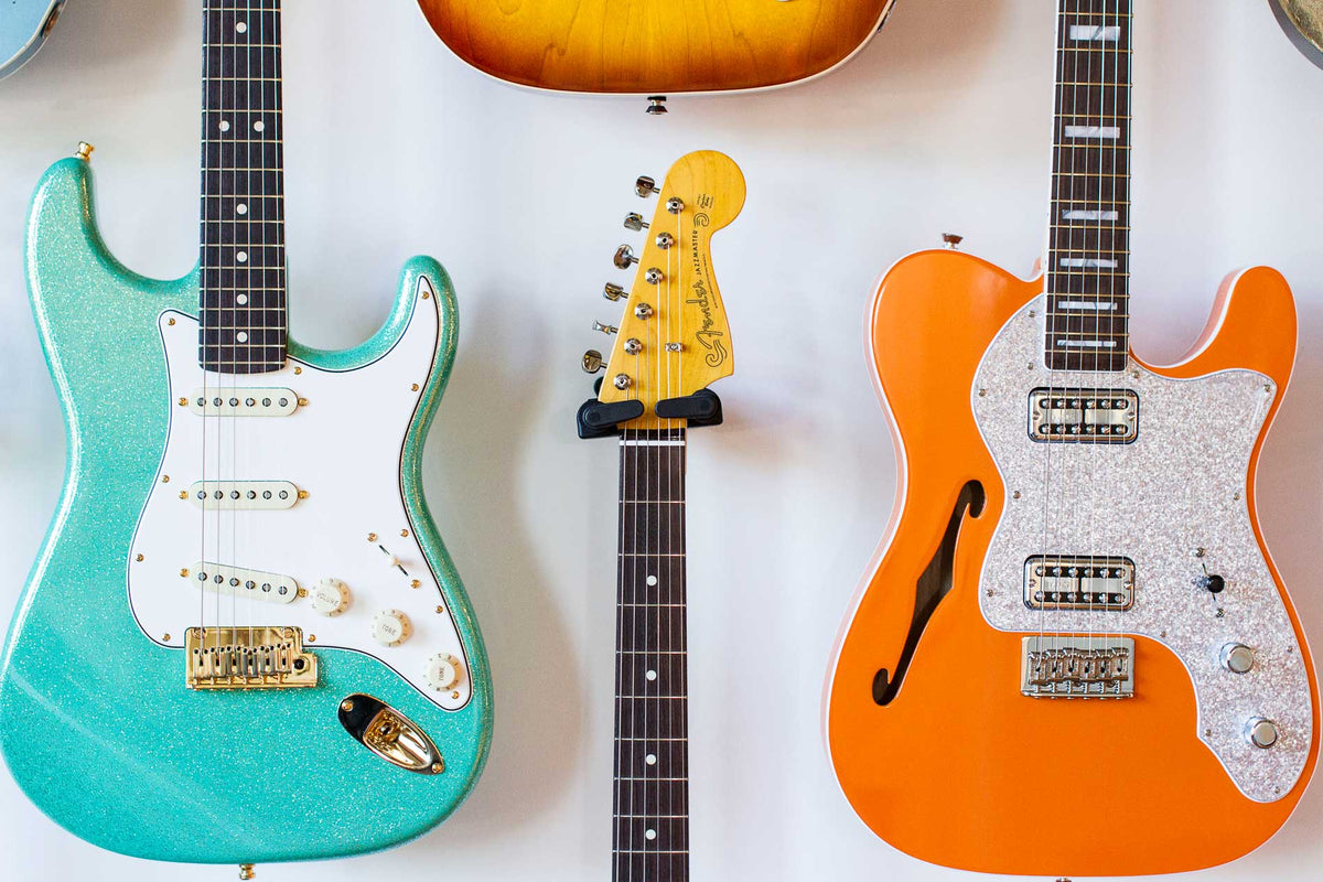 Teal and orange fender electric guitars hanging on a white wall.