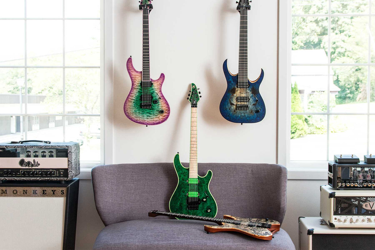 Pink, green, and blue Mayones electric guitars hanging over a grey chair.